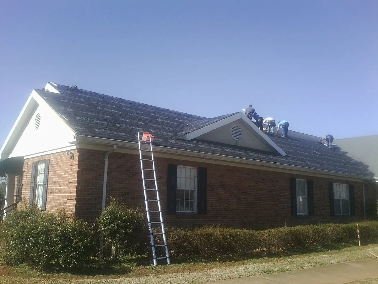 Crew tearing shingles off a brick ranch roof with a ladder set — Emergency Roof Repair work by our crew in White Mills