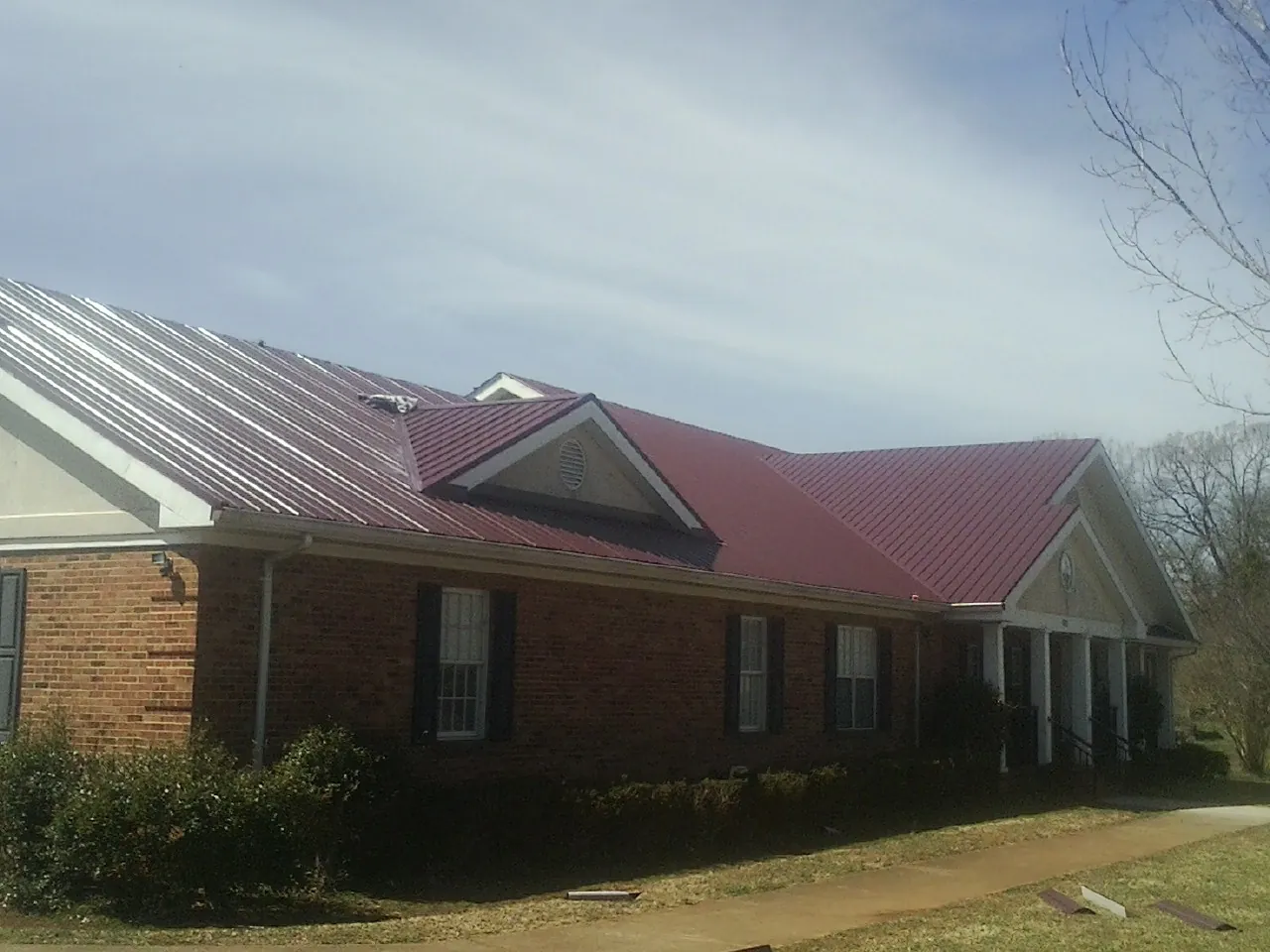 Red metal roof with gabled entries on a long brick building, from a Hail Damage Roof Repair job in White Mills