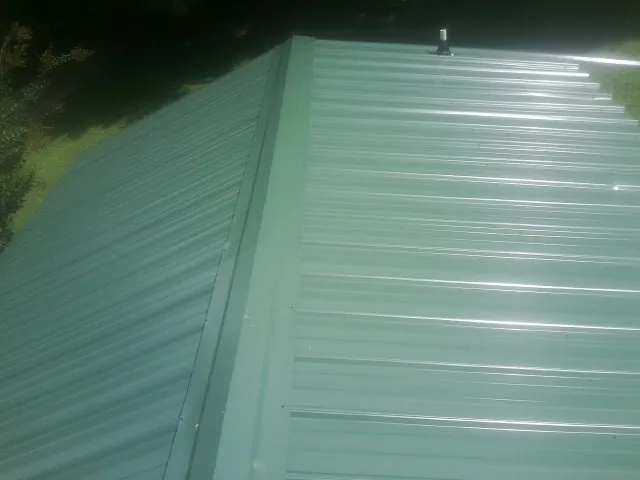 New green metal panels meeting at the ridge of a roof — Flat Roof Repair work by our crew in White Mills