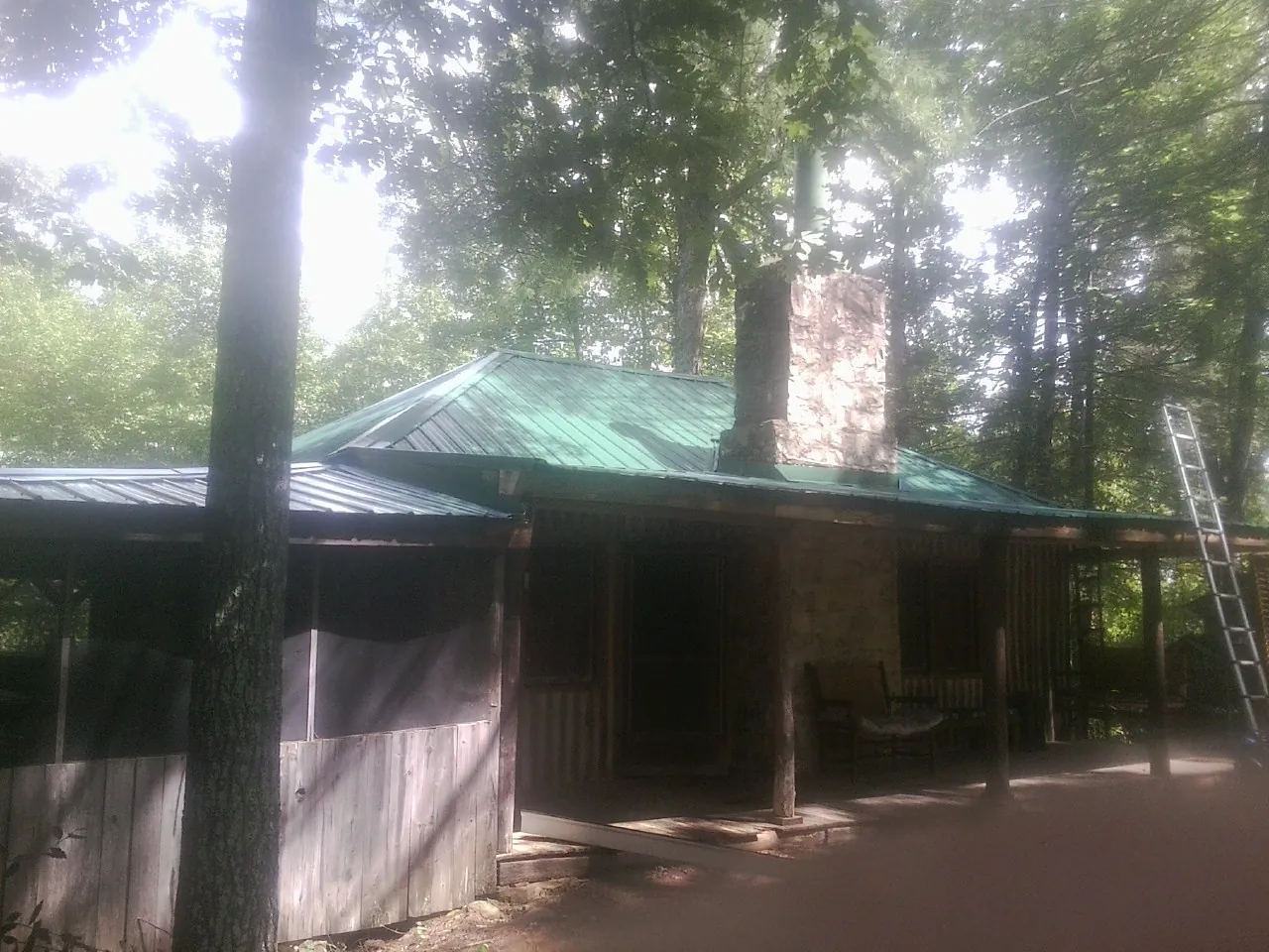 Green metal roof and stone chimney above a log cabin porch in White Mills