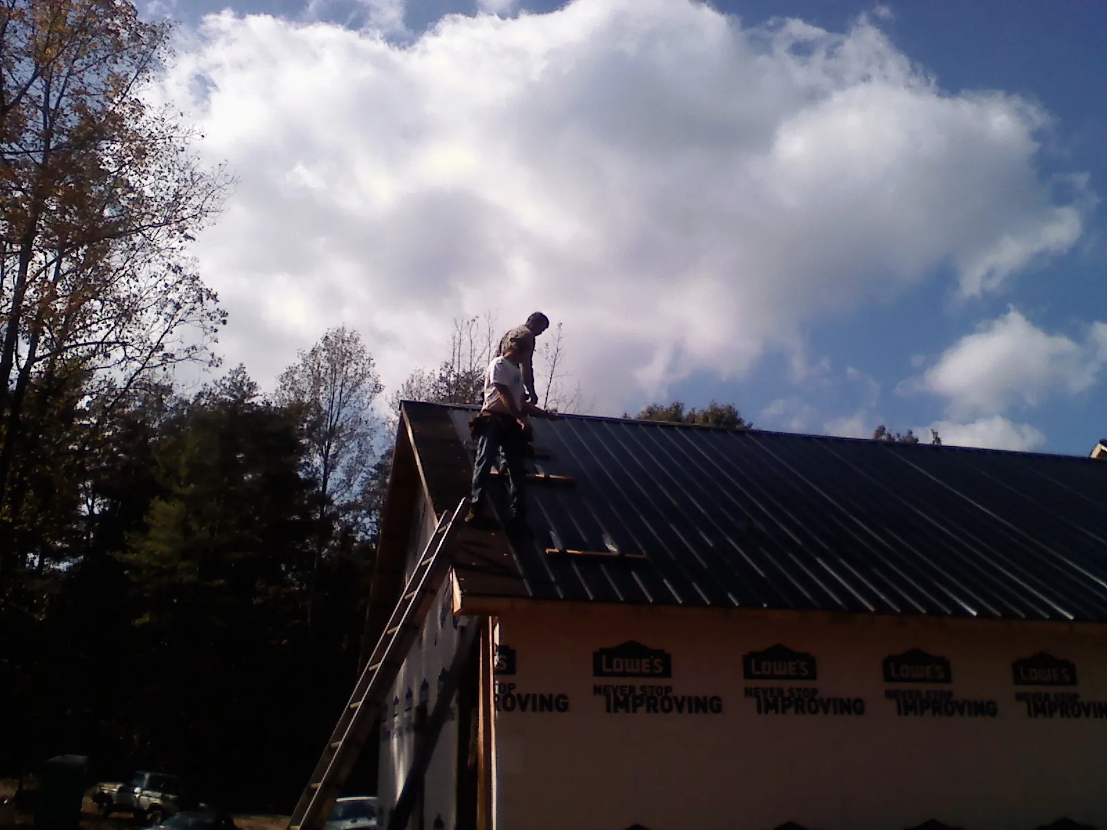 Roofer fastening dark metal panels high against a cloudy sky, from a Roof Inspection job in White Mills
