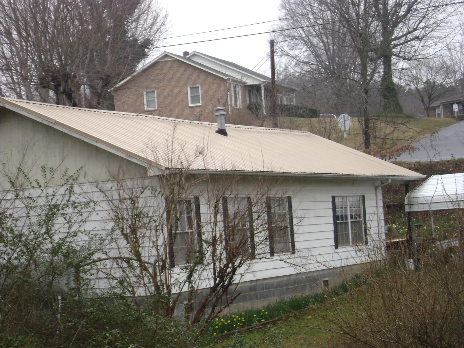 Tan metal roof on a white sided house set into a hillside — Commercial Roofing by Roofing Brothers in White Mills